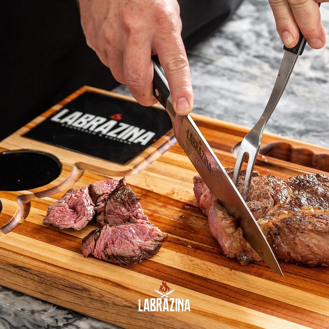 Mãos cortando picanha grelhada sobre tábua de madeira nobre Labrazina